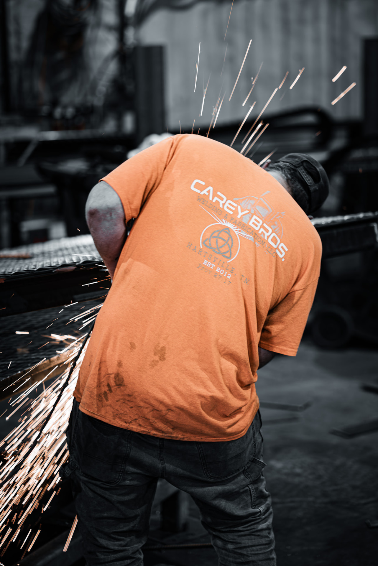 Carey Brothers crew member in a branded orange shirt grinding steel with sparks flying