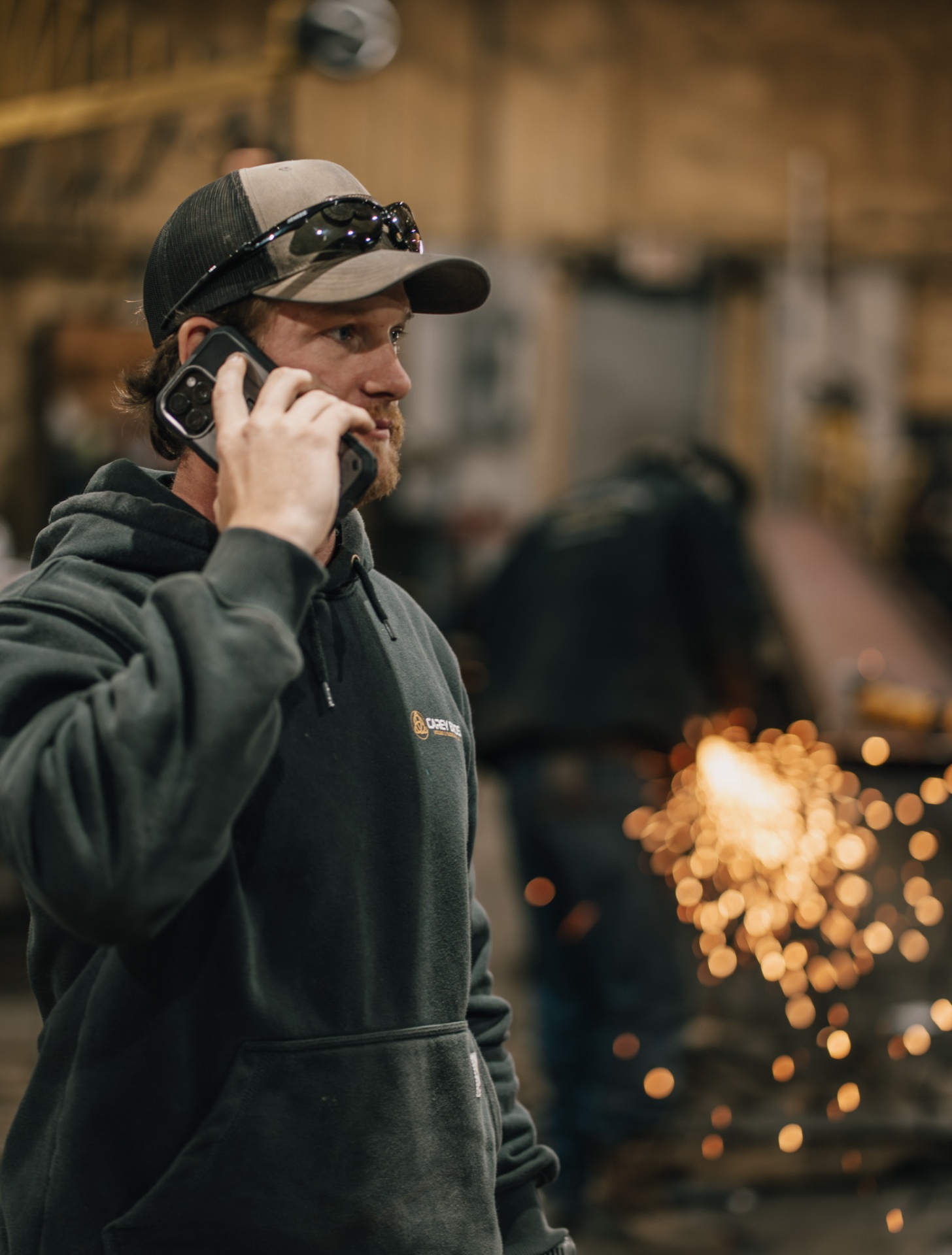 Tradesman on his cell phone in the shop while work continues behind him