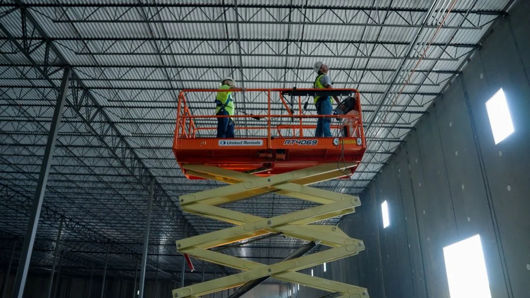 Two electricians on a scissor lift in a commercial warehouse