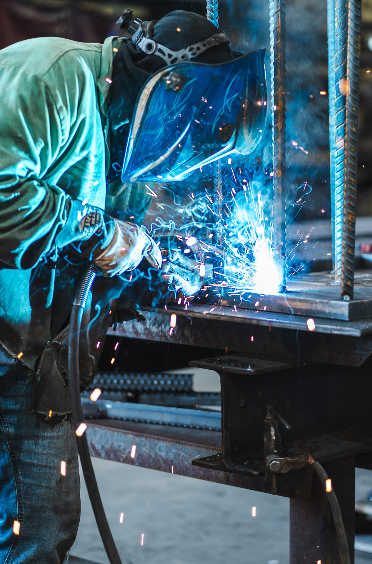 Carey Brothers welder in a helmet welding rebar to a steel plate with blue sparks